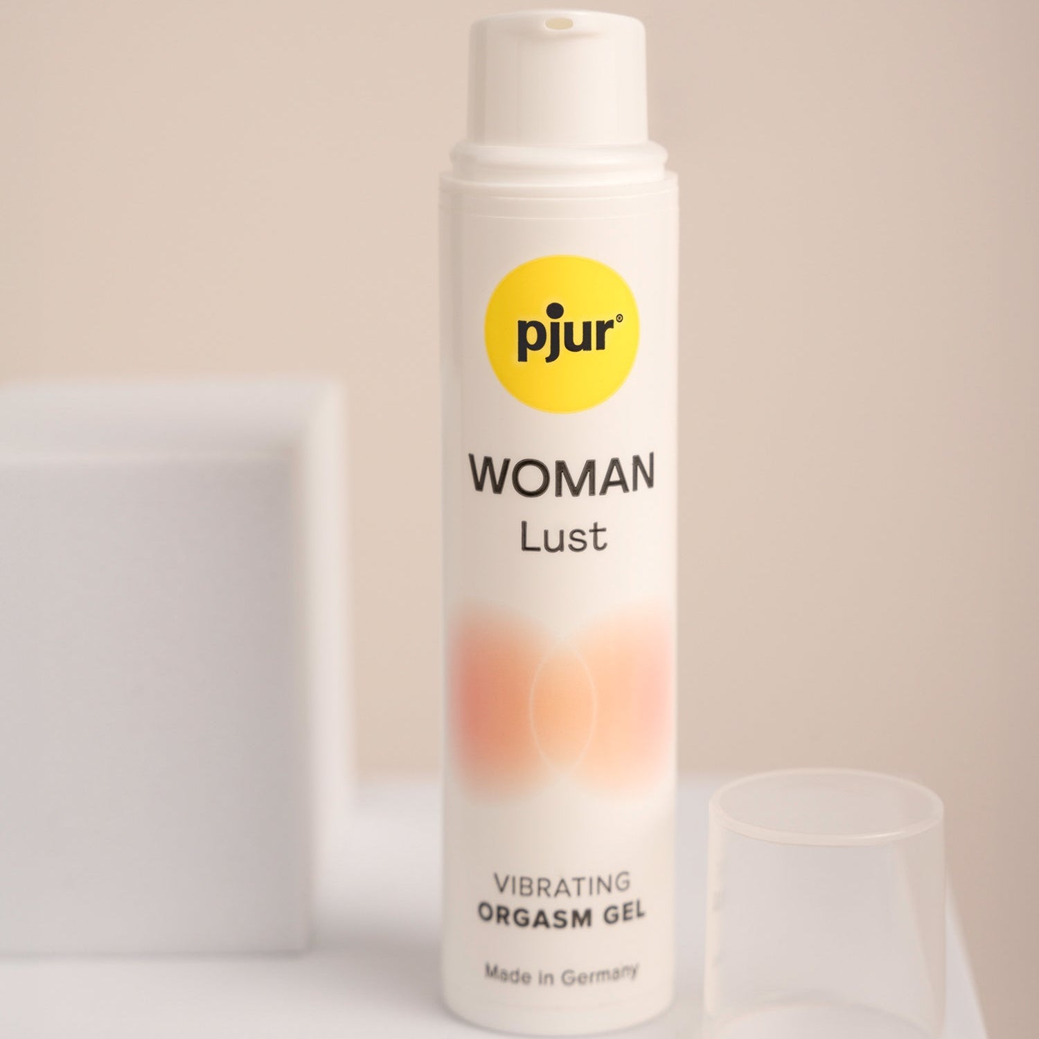 A bottle of Pjur Lust Intense water-based organic gel, with a white and yellow label, positioned on a surface with a glass next to it.
