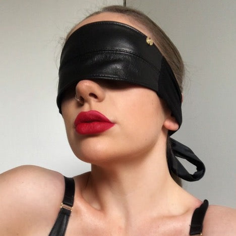 Person wearing a black leather blindfold and top against a neutral background