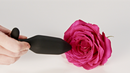 Hand holding Onyx Vibrating Butt Plug against a pink rose